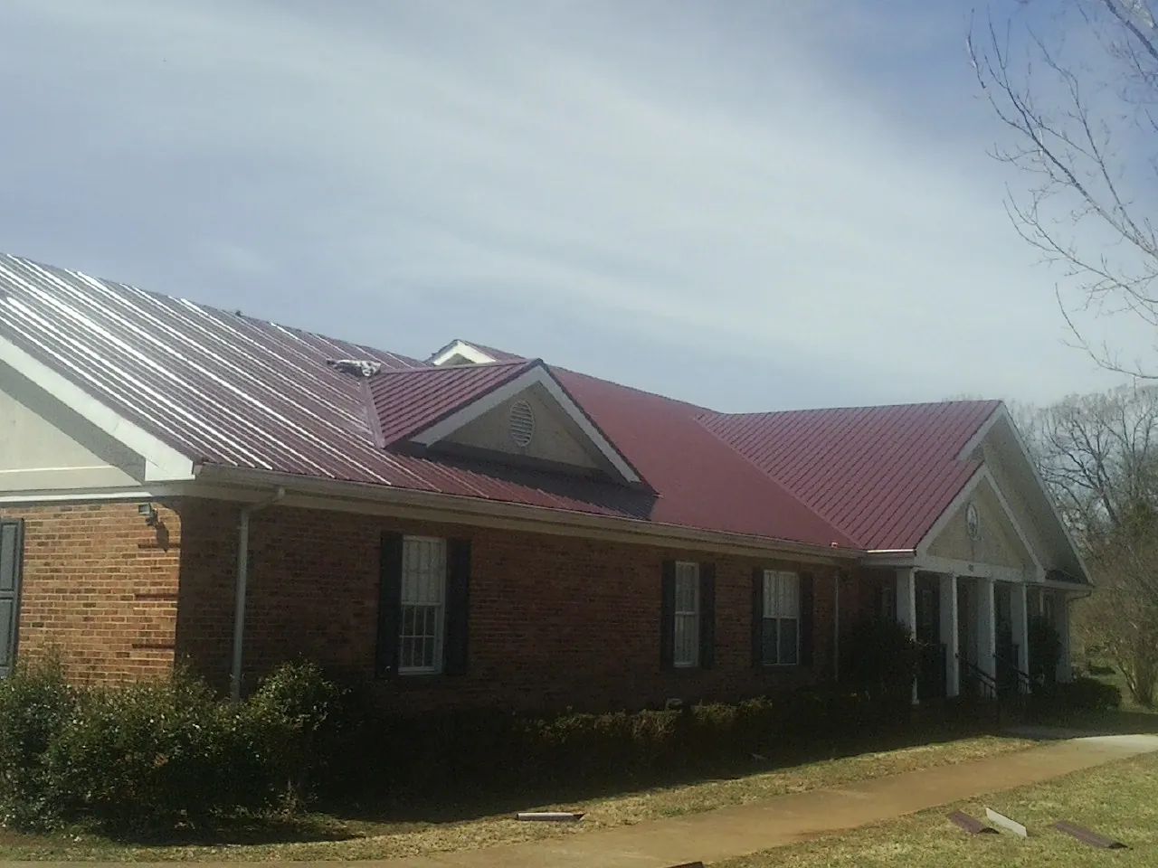 Red metal roof with gabled entries on a long brick building, from a Hail Damage Roof Repair job in Neilton