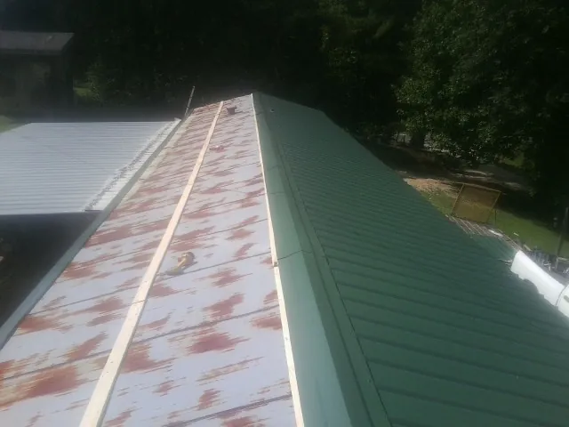 Old rusted panels beside newly installed green metal roofing — Wind Damage Roof Repair by Roofing Brothers in Neilton