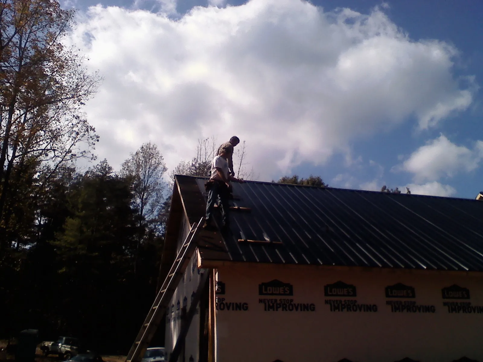 Roofer fastening dark metal panels high against a cloudy sky, from a Roof Inspection job in Neilton