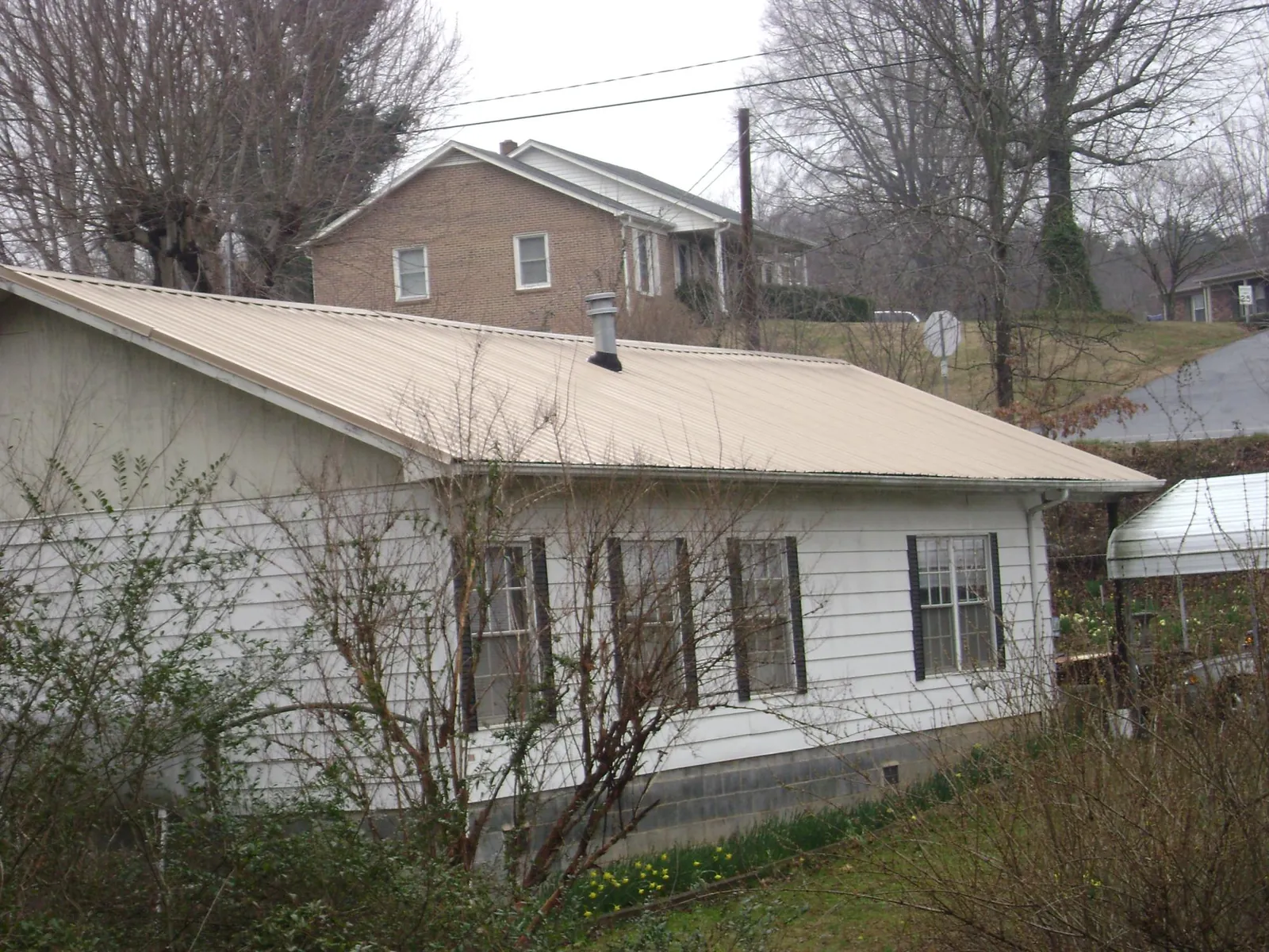 Tan metal roof on a white sided house set into a hillside — Commercial Roofing by Roofing Brothers in Neilton